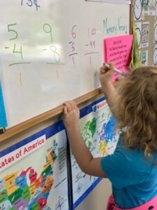 A student writes math problems on a dry erase board.